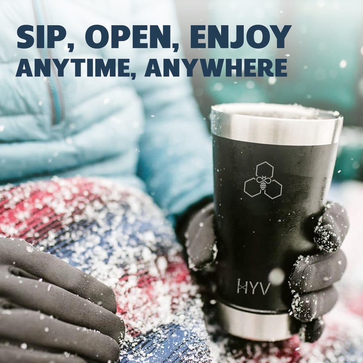 Gloved hands holding a dark HYV OpenFlow tumbler in falling snow